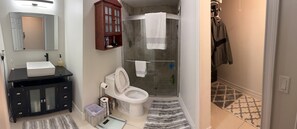 A bathroom with a white sink, black vanity, a glass shower enclosure, and a towel rack with towels.