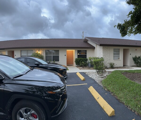 A building with a parking lot, a driveway leading to the entrance, and a small garden area.