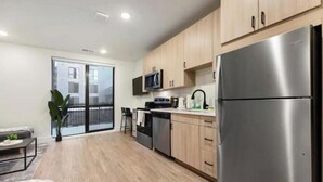 Eine moderne Küche mit Edelstahlgeräten, Holzschränken und einer Glastür zum Balkon.