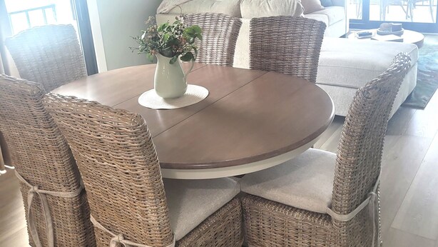 Un coin repas avec des chaises et une table ronde en osier, un canapé en osier et une plante décorative.