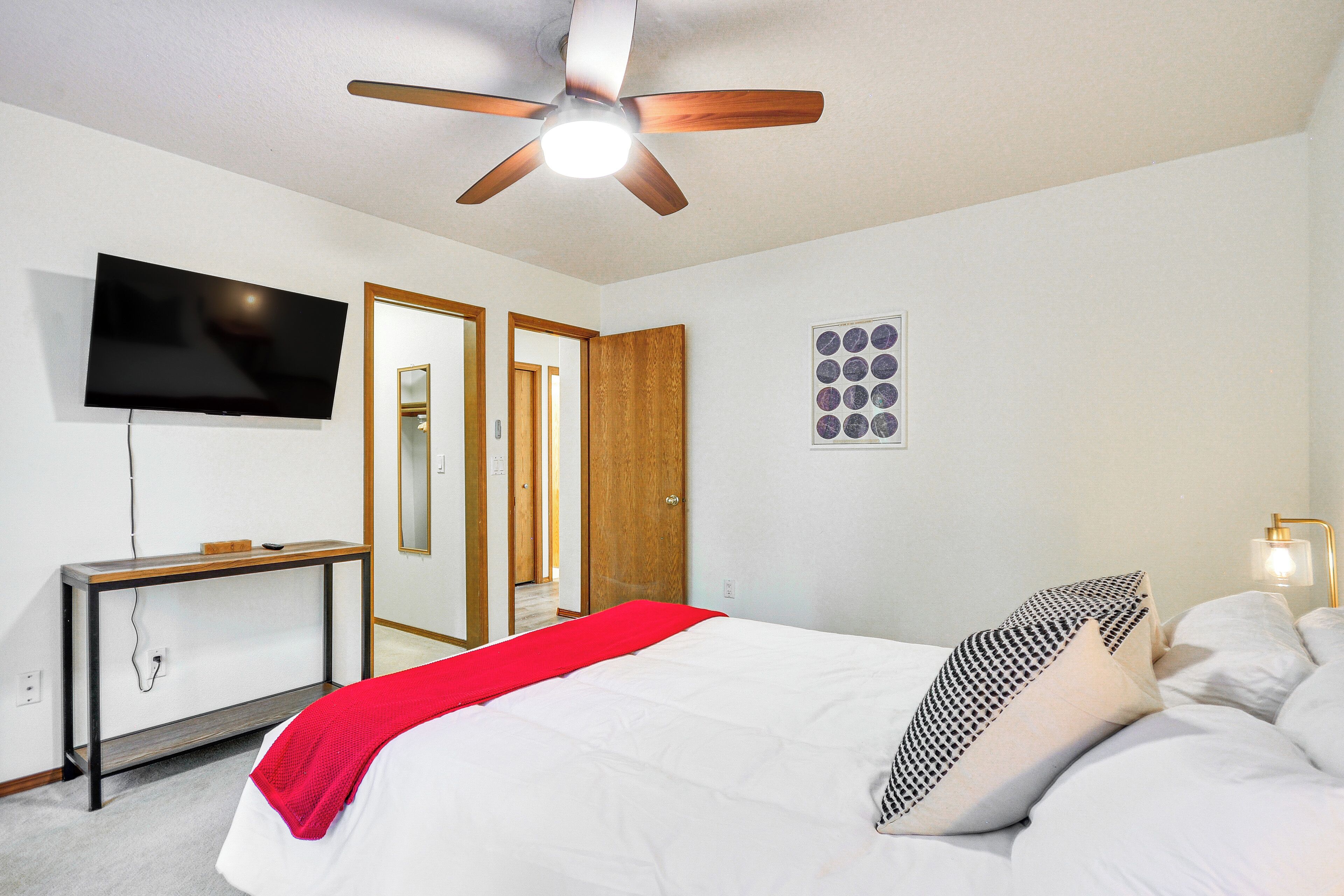 A bedroom with a bed, a ceiling fan, a TV, a bedside table, and a nightstand.