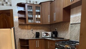 A kitchen with wooden cabinets, a stainless steel refrigerator, a microwave, a coffee maker, and a gas stove. - Dafrican BnB  (Kigali)