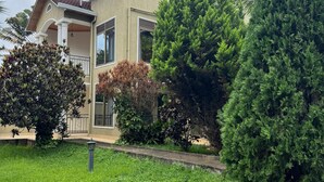 A two-story house with a covered porch, a well-maintained lawn, and several mature trees. - Dafrican BnB  (Kigali)