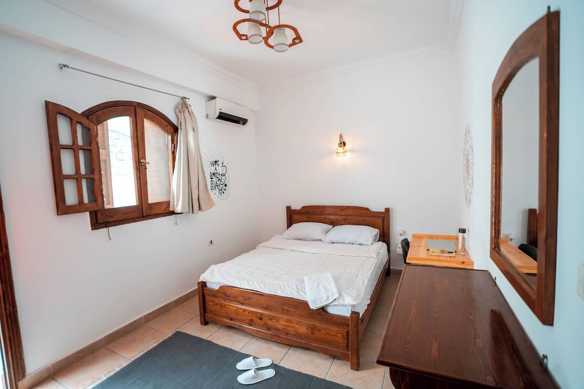 Un dormitorio con una cama de madera, una mesita de noche, un espejo, una lámpara de pared y una ventana con cortinas.