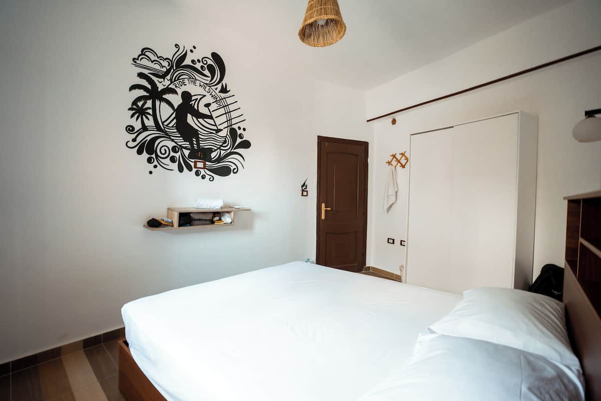 Un dormitorio con cama, decoración en la pared, una puerta y una estantería con objetos.