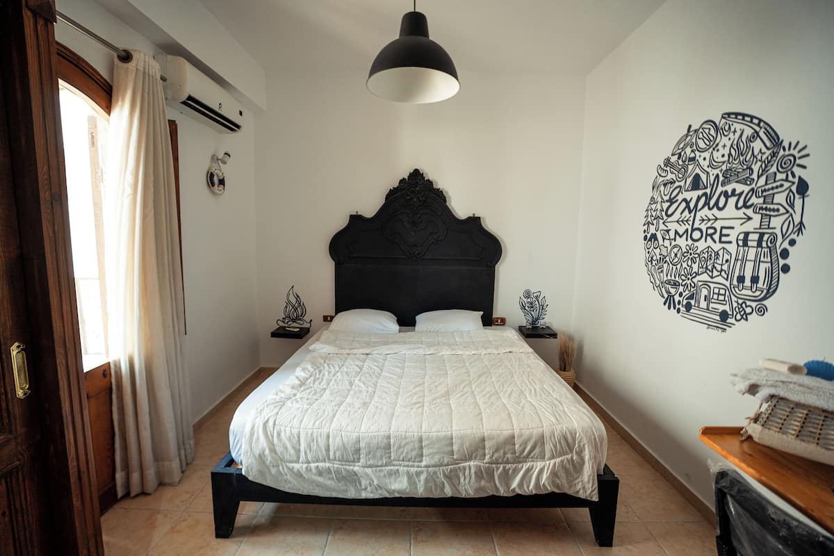 Un dormitorio con una cama grande, cabecera oscura, un adorno en la pared y una mesita de noche de madera.