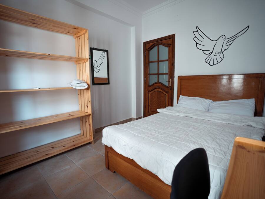 Ein Schlafzimmer mit einem hölzernen Bett, einer Holzregaleinheit, einem gerahmten Bild und einer Wandsticker-Vogel.