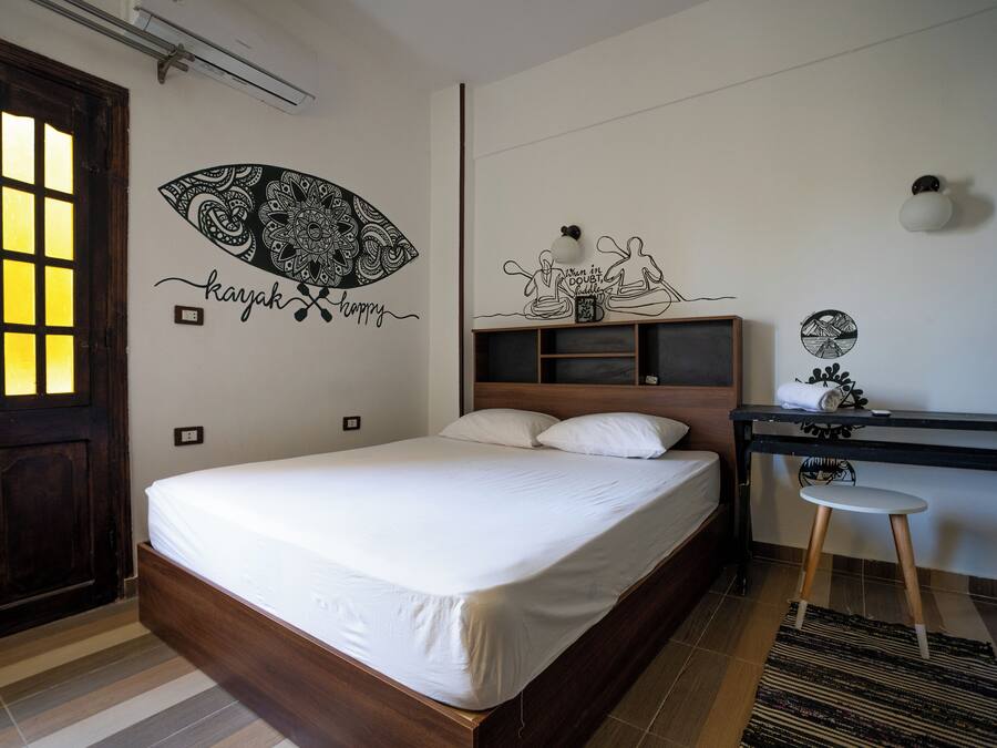Een slaapkamer met een houten bed, een bureau met stoel, een muur met decoratieve kunst en een deur met raam.