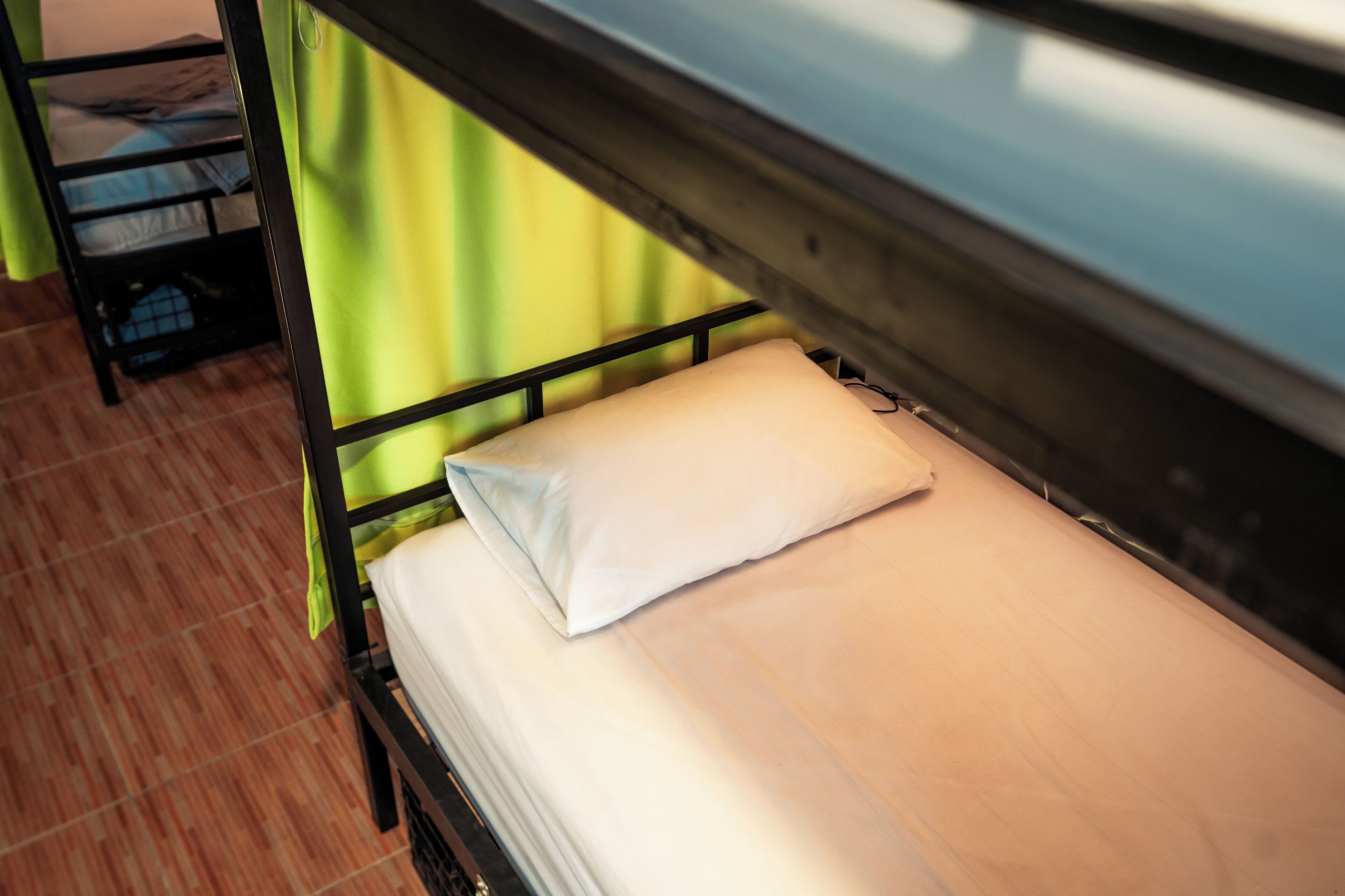 Una cama litera con almohada y colchón, una cortina verde y un piso de baldosas.