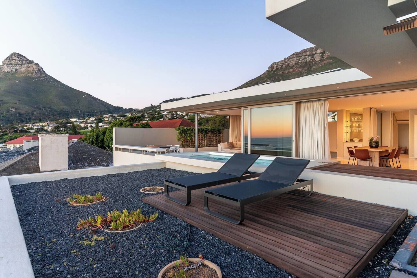 A modern outdoor deck with a pool, lounge chairs, and a view of the ocean.