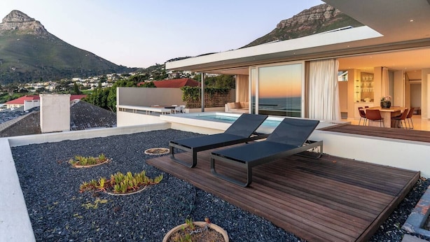 A modern outdoor deck with a pool, lounge chairs, and a view of the ocean. - Aquatic Penthouse - Coastal Luxury & Rooftop Views (Cape Town)