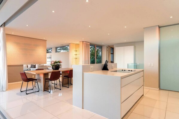 Cocina moderna con una isla central, comedor con sillas y vistas al exterior.