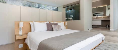 A modern bedroom with a large bed, bedside tables, a built-in wardrobe, and a bathroom visible through a glass door.