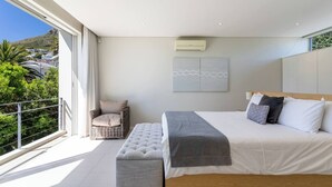 Une chambre moderne avec un grand lit, un banc, une chaise et une vue sur la verdure et les bâtiments.