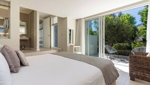 Une chambre moderne avec un grand lit, une salle de bain et un balcon agrémenté de meubles en osier.