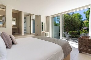 Un dormitorio moderno con una cama grande, un baño y un balcón con mobiliario de mimbre.