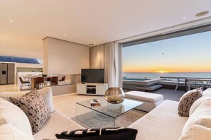 Een moderne hotelkamer met balkon en uitzicht op zee, een eethoek en een zithoek met een flatscreen televisie.
