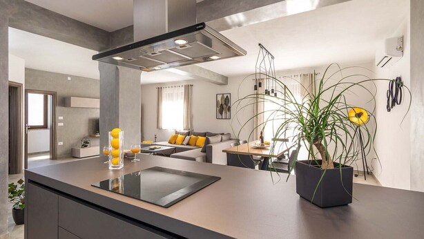 A modern kitchen with a central island, a dining area with a sofa, and a living room with a large window. - Villa Leonardelli in Galizana (Galizana)