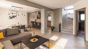 A spacious living area with a sofa, coffee table, and dining table. There is a kitchen in the background with bar stools. - Villa Leonardelli in Galizana (Galizana)