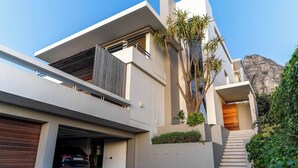 Uma casa moderna de dois andares com garagem e uma escadaria que leva ao andar superior, com uma montanha ao fundo.