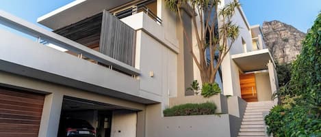 A modern two-story house with a garage, a staircase leading to the upper level, and a mountain in the background.