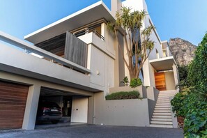 Ett modernt hus i två våningar med ett garage, en trappa som leder upp till övre våningen och ett berg i bakgrunden.