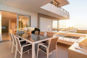 Un comedor moderno con una mesa de vidrio y sillas blancas, con vista a un balcón frente al océano.