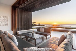 A modern outdoor seating area with a view of the sunset over the ocean.