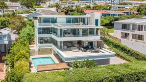Ein modernes, zweistöckiges Haus mit Pool, umgeben von üppiger Vegetation und weiteren Wohngebäuden.