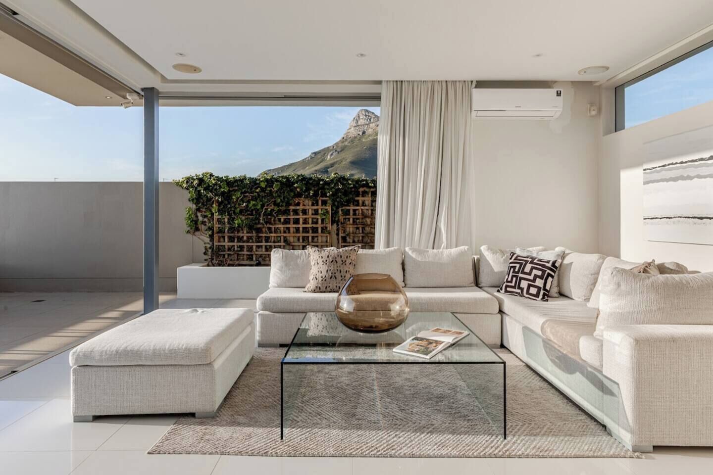 A modern living room with a glass coffee table, a sofa set, and a view of a mountain.