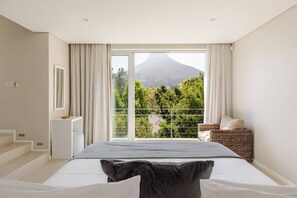 Une chambre avec un lit, une vue sur la verdure et une montagne, et un balcon avec un fauteuil en osier.