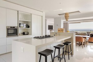 A modern kitchen with a central island, bar stools, and a view of the ocean.
