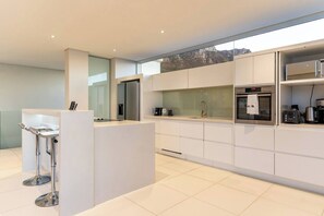 A modern kitchen with a central island, built-in appliances, and a large window overlooking a mountainous landscape.