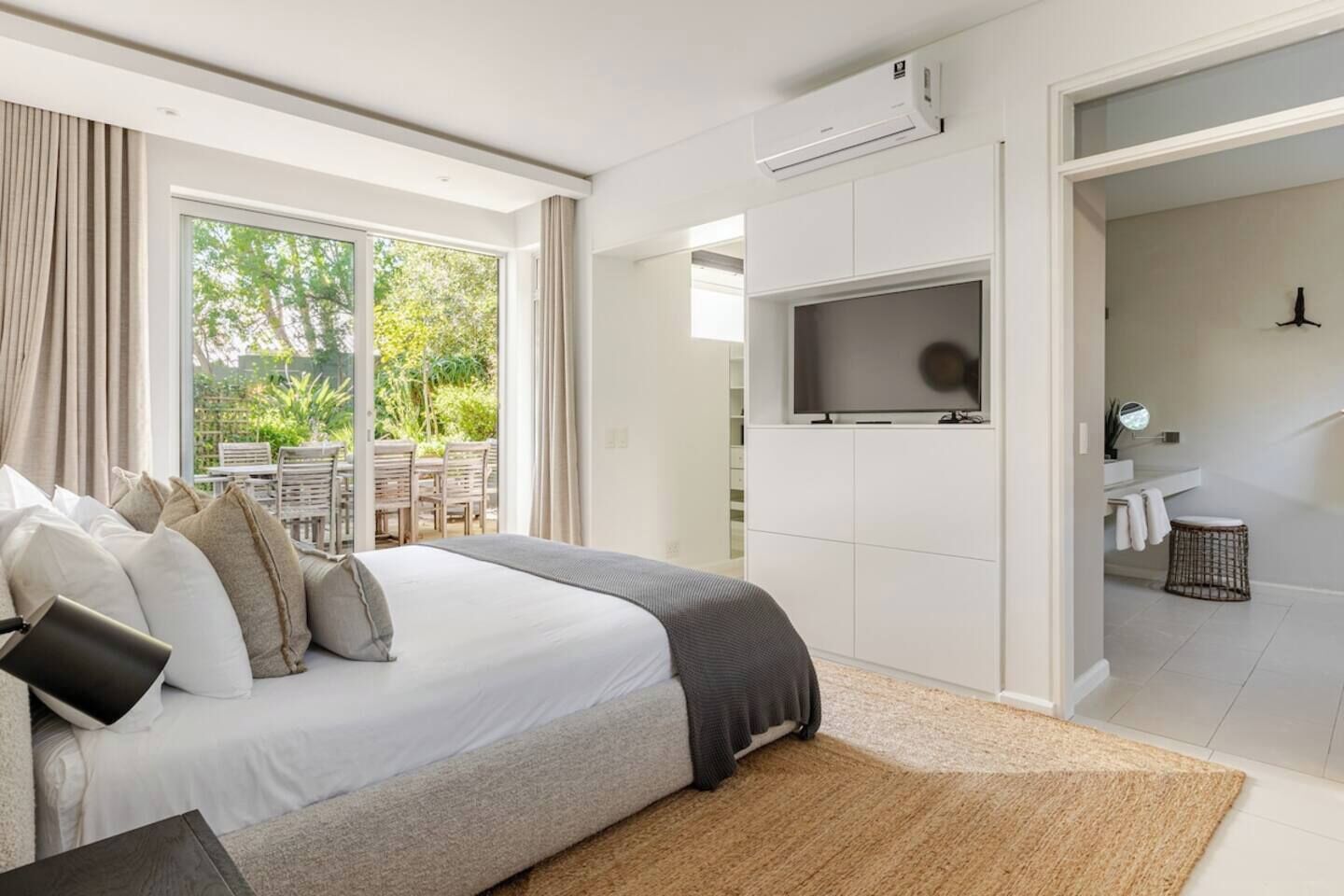A modern bedroom with a large bed, a TV mounted on the wall, and a view of the outdoors through the window.