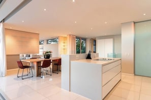 A modern kitchen with a central island, dining area with chairs, and a view of the outdoors.