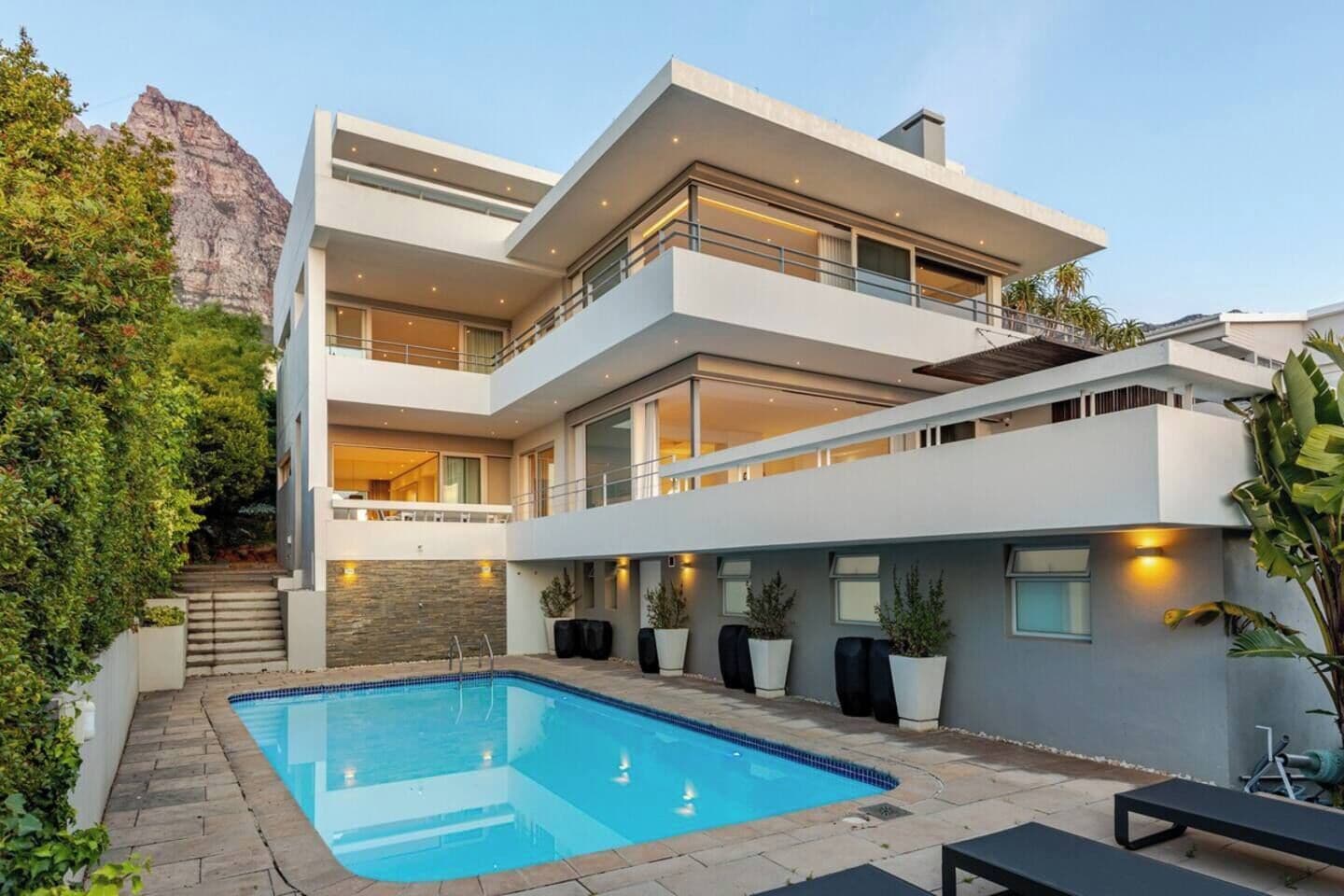 A modern multi-story house with a swimming pool, outdoor seating, and a view of a mountain.