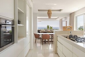 A modern kitchen with a view to the sea, a dining area, and a large window.
