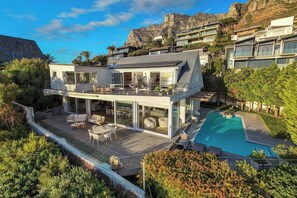 A modern two-story house with a pool, deck, and mountain backdrop.