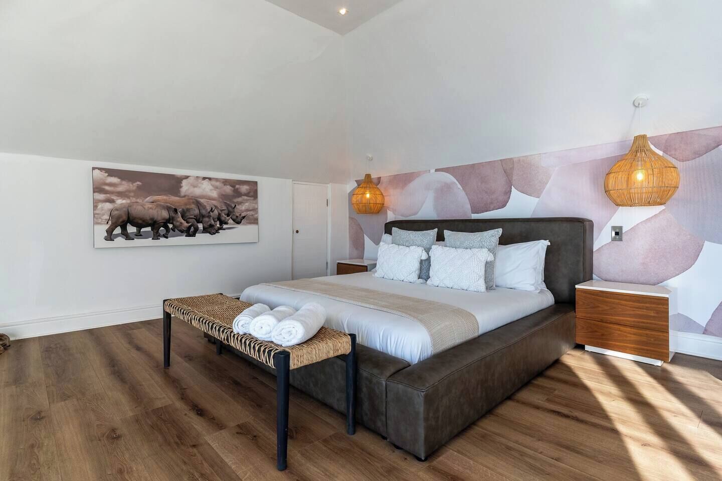 Een slaapkamer met een groot bed, een bank met handdoeken, een wandlamp en een schilderij van neushoorns.
