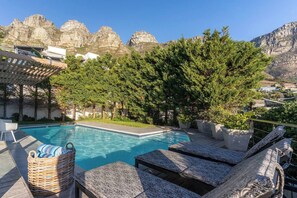 A swimming pool with lounge chairs, a pergola, and a view of rocky mountains.