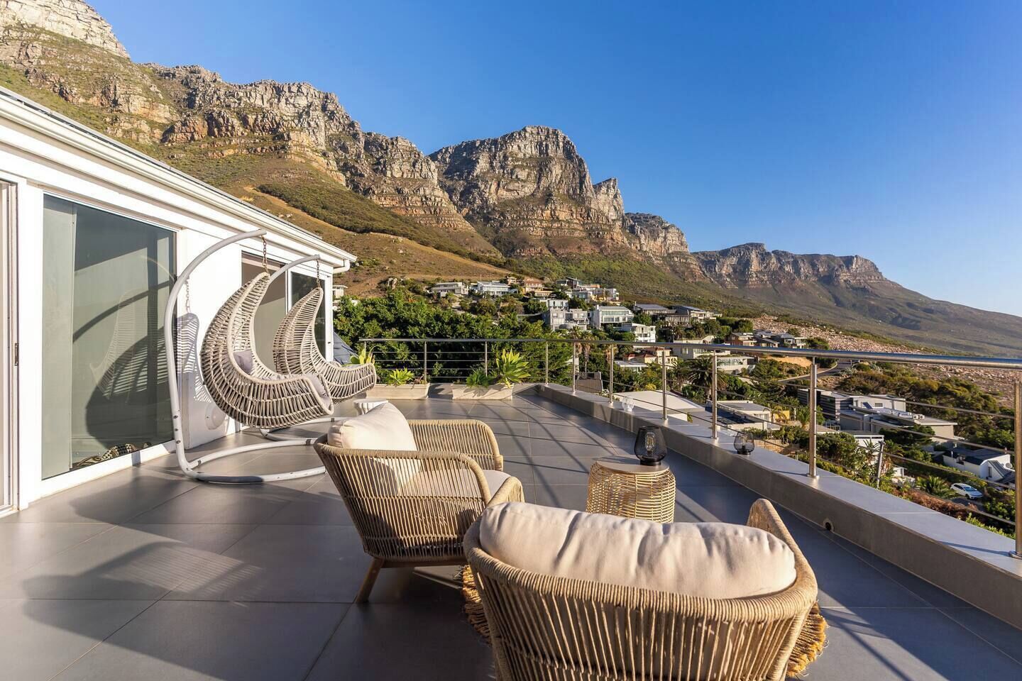 A balcony with wicker furniture, a glass door, and a view of a town and mountains.