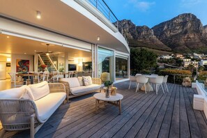 A modern outdoor living space with a wooden deck, furnished seating, and a view of mountains in the background.