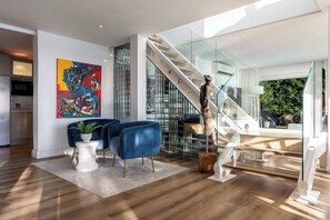 A modern living room with a staircase, a colorful abstract painting, and a potted plant.