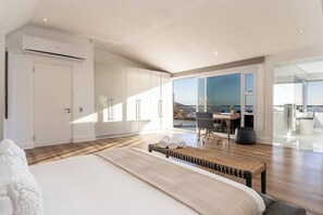 A modern bedroom with a large bed, a desk, and a view of the outdoors.