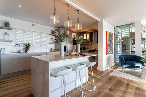 A modern kitchen with a central island, bar stools, pendant lighting, and a view into the dining area.