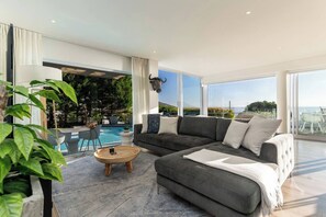 A modern living room with a grey sofa, a coffee table, and a view of a pool and outdoor area.