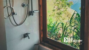 Une salle de bain avec douche, une fenêtre donnant sur un paysage verdoyant et des montagnes, et un mur carrelé.