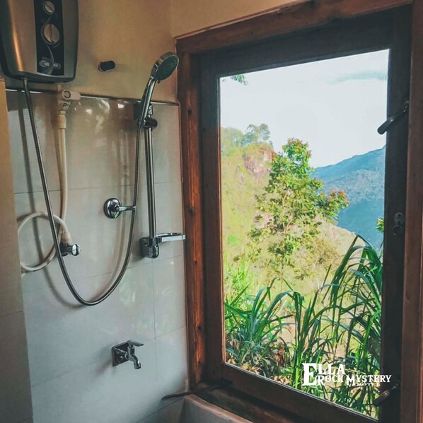 Une salle de bain avec douche, une fenêtre donnant sur un paysage verdoyant et des montagnes, et un mur carrelé.