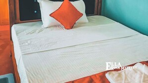 Un lit bien fait, avec une literie blanche et un seul oreiller orange, une tête de lit en bois et un mur d’accent de couleur turquoise.