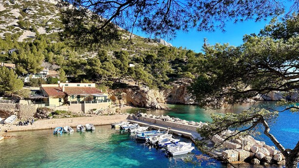 Una zona costera con aguas turquesas cristalinas, un puerto deportivo con barcos y un edificio con techo de tejas rojas.